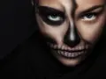 Frau mit Totenkopf-Halloween-Make-up, dunkler Hintergrund.