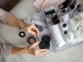 Hände sortieren Kosmetik in einem transparenten Organizer mit Pinseln, Puderdosen und Cremes.