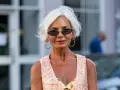 Frau mit weißem Kurzhaarschnitt, Sonnenbrille und auffälligem Schmuck.