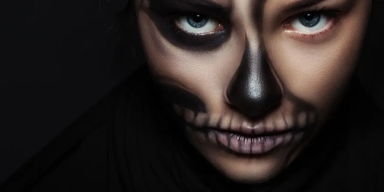 Frau mit Totenkopf-Halloween-Make-up, dunkler Hintergrund.