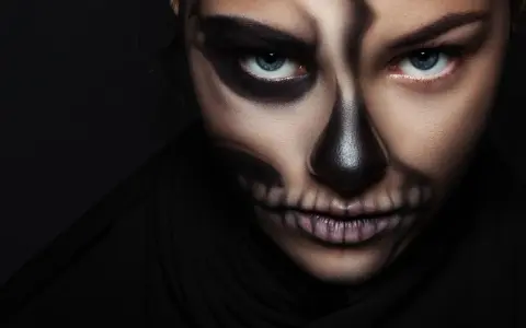 Frau mit Totenkopf-Halloween-Make-up, dunkler Hintergrund.