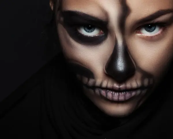 Frau mit Totenkopf-Halloween-Make-up, dunkler Hintergrund.
