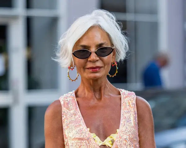 Frau mit weißem Kurzhaarschnitt, Sonnenbrille und auffälligem Schmuck.