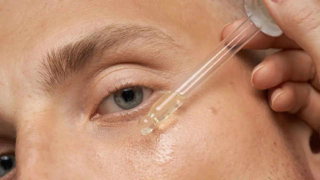 Pipette gibt Öl auf trockene, schuppige Gesichtshaut neben dem Auge.